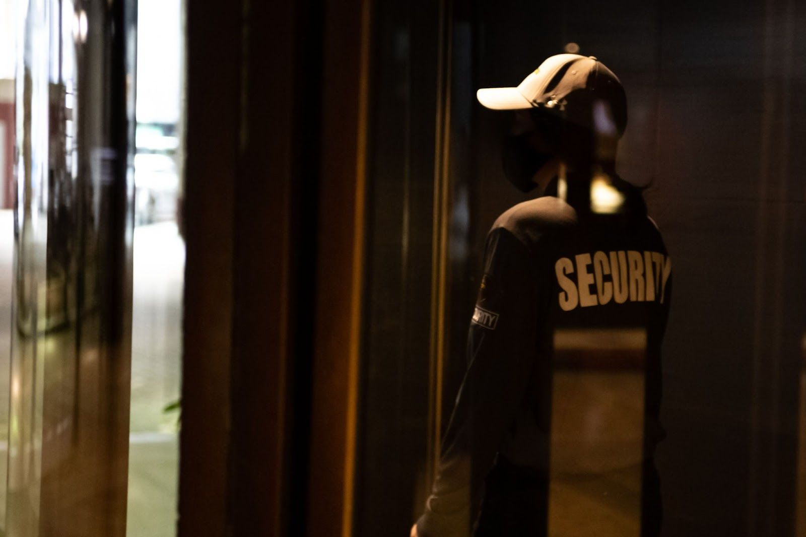 A man in a black jacket with 'SECURITY' in white letters on the back is looking at a door.