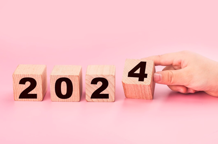 Wooden blocks arranged to show the year “2024,” with a hand placing the final block displaying the number 4.